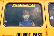 Little Sad Boy Kid Student In Protective Face Mask Looking Out Of School Yellow Bus Window. New Nor