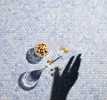 Directly Above Shot Of Shadow Hand Reaching Towards Pistachios And Martini Glass On Blue Background