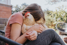 Woman Embracing Chicken While Sitting On Chair In Backyard
