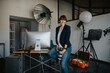 © Westend61 - Happy female professional holding camera while sitting on desk at studio