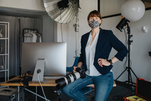 Female Photographer Sitting With Camera On Desk In Studio During Pandemic
