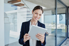 Smiling Female Real Estate Agent With Digital Tablet Standing By Glass Wall