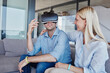 © Westend61 - Cheerful blond woman looking at man wearing virtual reality simulator sitting in living room
