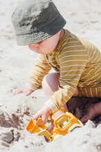 Boy Sitting On Sand Playing With Toy Car At Beach