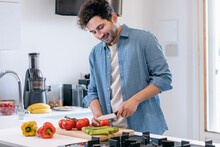 Smiling Mid Adult Man Cutting Tomatoes In Kitchen At Home