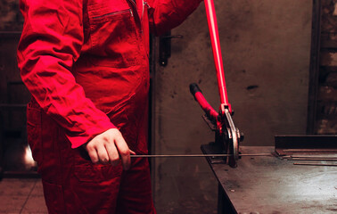 Worker wearing red overalls using pincers or plier wrenches to cut a steel wire or bar in workshop of a factory or plant