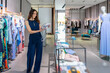 © Westend61 - Young woman holding purse while standing near clothes rack in boutique