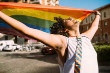 Young Male Activist Looking Up While Holding Rainbow Flag On Street