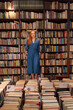 © Westend61 - Woman standing on ladder amidst books in library