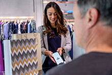 Woman Paying Contactless Through Smart Phone At Clothes Store