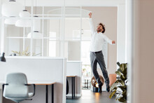 Excited Businessman Jumping With Hand Raised In Office