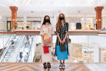 Female Friends With Protective Face Masks Holding Shopping Bags In Mall