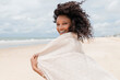 © Westend61 - Smiling young woman with towel looking over shoulder at beach