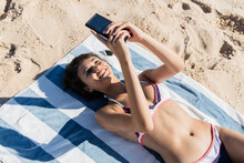 Smiling Young Woman Using Mobile Phone While Relaxing At Beach