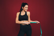 © Westend61 - Happy slim sportswoman measuring waist in front of maroon background