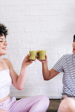 Friends Toasting Smoothie In Front Of White Brick Wall