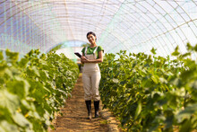 Smiling Female Farmer With Digital Tablet Standing At Greenhouse