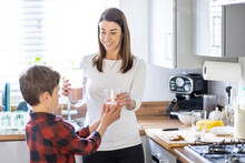 Smiling Mother Giving Glass Of Milkshake To Son In Kitchen At Home