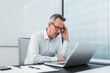 © Westend61 - Businessman with head in hand sitting with laptop at desk