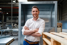 Smiling Businessman With Arms Crossed Leaning On Wooden Pallet