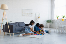African American Mother And Granny Playing Building Blocks Game With Girl On Floor In Spacious Living Room