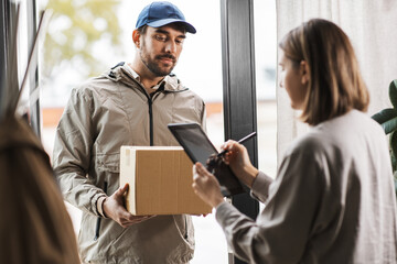 shipping, mail service and people concept - delivery man with parcel box and customer signing digital form in tablet pc computer at home