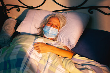 sick older woman with face mask lying in bed looking at a ray of sun coming through the window