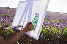 Young Woman Painting Lavender Flowers On Canvas In Field