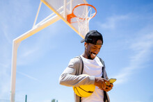 Smiling Man With Basketball Using Mobile Phone At Park