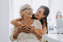 Cheerful Woman Hugging Grandmother Sitting In Kitchen