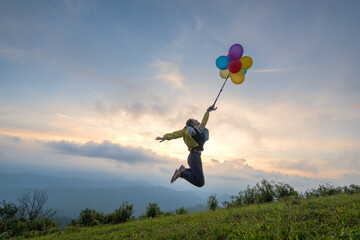 Happy woman with colorful air balloons jumping on summer field at sunset on nature in summer