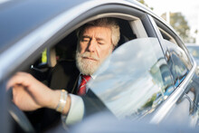 Mature Businessman Looking At Wristwatch While Driving Car In City