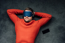 Male Professional Napping With Eye Mask While Listening Music Through Headphones At Workplace