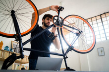 Man With Laptop Rotating Bicycle Pedals At Home