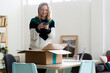 © Westend61 - Smiling woman taking photo of package box through mobile phone at home