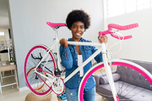 Smiling Young Woman Carrying Bicycle At Home