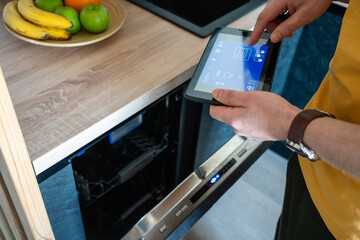 Man operating oven through digital tablet in kitchen