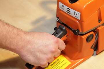 Poster - A man's hand holds the handle and pulls the chainsaw throttle trigger of the close-up - woodcutting tools equipment maintenance