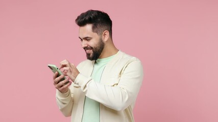 Wall Mural - Young bearded brunet man 20s wears white shirt hold use mobile cell phone typing browsing swipe chatting send sms doing online shopping isolated on plain pastel light pink background studio portrait