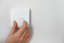 Woman Turning Down Heating Thermostat To Save Money.