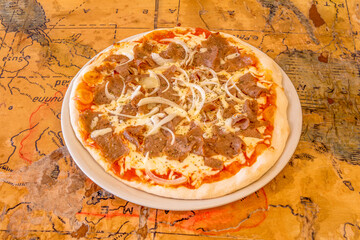 Freshly made pizza with ingredients and kebab or shawarma meat with cheese, peppers and lots of onions and cooked in a stone oven.