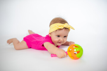 Wall Mural - cute, beautiful little girl in a pink bodysuit
 and a bandage lies on a white background, smiles and gnaws toys. beautiful baby. teeth are erupting. portrait of a baby. portrait of a beautiful girl