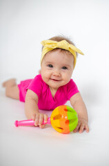 Wall Mural - cute, beautiful little girl in a pink bodysuit
 and a bandage lies on a white background, smiles and gnaws toys. beautiful baby. teeth are erupting. portrait of a baby. portrait of a beautiful girl