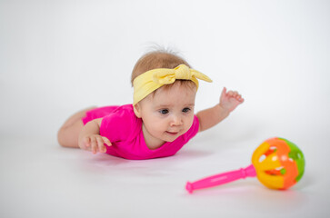 Wall Mural - cute, beautiful little girl in a pink bodysuit
 and a bandage lies on a white background, smiles and gnaws toys. beautiful baby. teeth are erupting. portrait of a baby. portrait of a beautiful girl