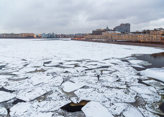 Wall Mural - Winter view of the Neva River in the city center of St. Petersburg, Russia. Cracked ice floes on the surface of the water. Cold winter weather. Historical and modern buildings on the embankment.
