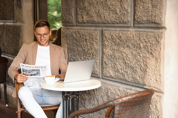 Poster - Handsome young man reading newspaper at table in street cafe