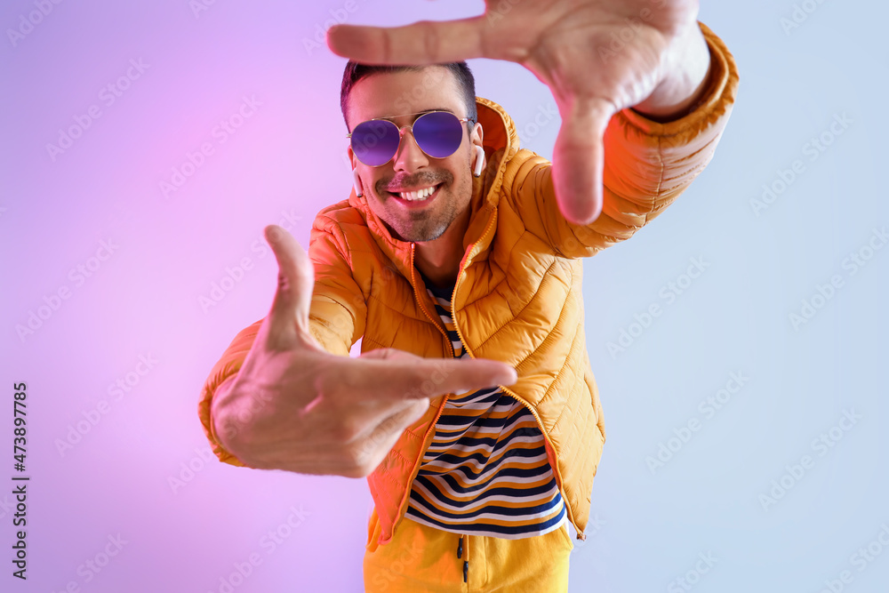 Stylish young man in sunglasses and yellow jacket on color background