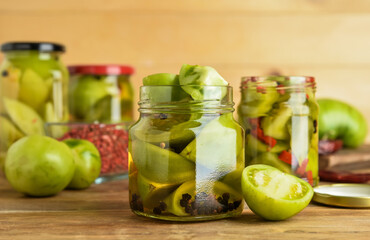 Jars with canned green tomatoes on wooden background