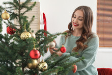 Young woman decorating Christmas tree in room