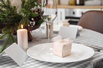 Plate with gift box and blank card on dining table decorated for Christmas celebration